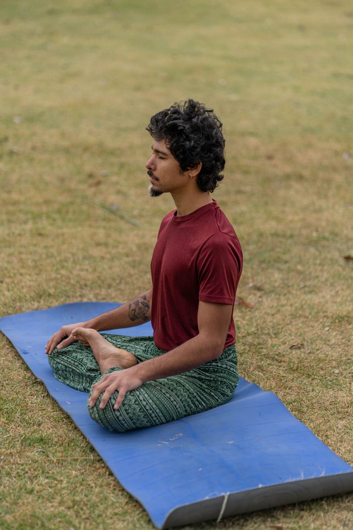 contact-img A man meditating in a relaxed posture on a blue yoga mat in a grassy field.