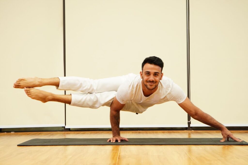A man balances in an advanced yoga pose on a mat indoors, showcasing strength and focus.