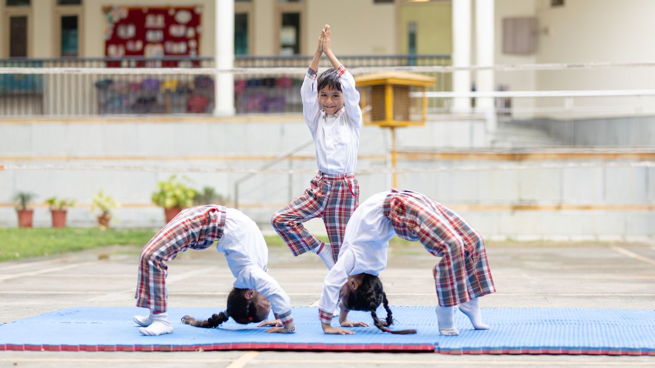 services-02 Three children performing yoga poses outdoors on a school playground.
