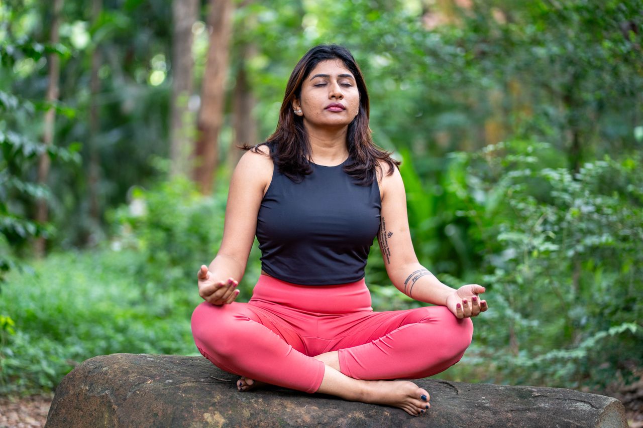 services-01 A woman practicing meditation outdoors surrounded by lush greenery.