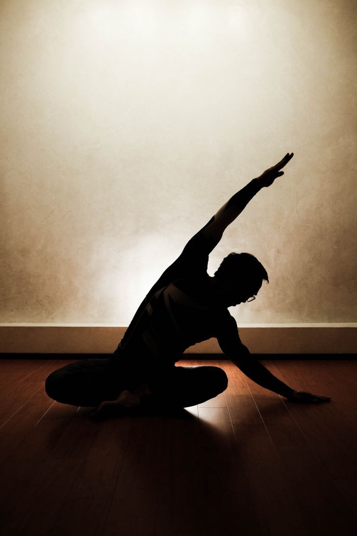 Silhouette of a person performing a yoga pose indoors with dramatic lighting.